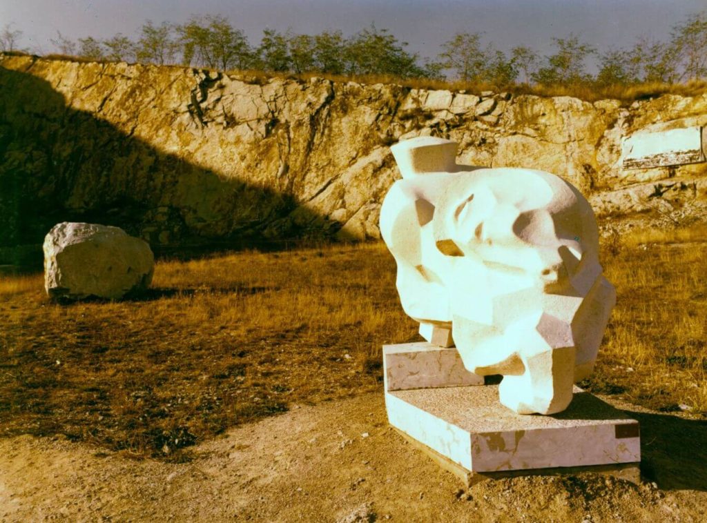 Stone statue in front of rock wall at Nagyharsányi Statue Park