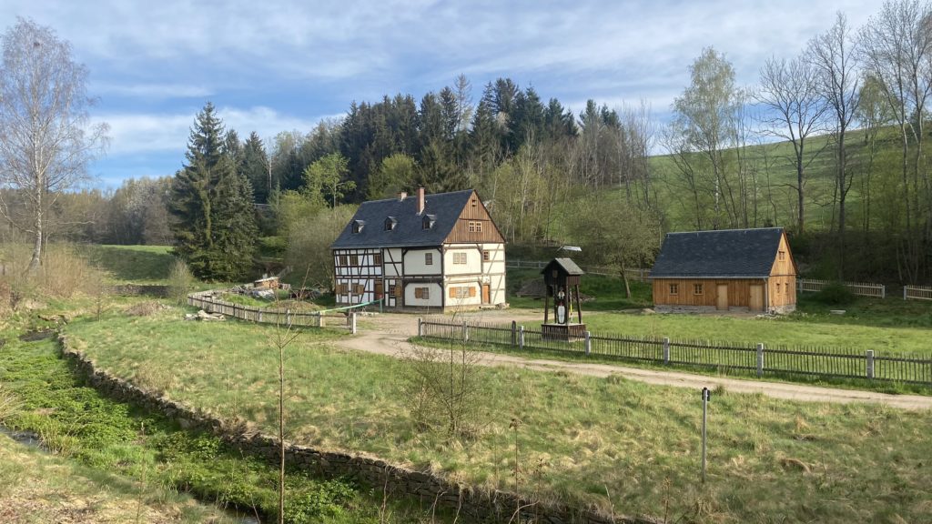 A landscape view around the town of Schneeberg with features of mining heritage - traditional house, a mining tunnel with a steep hill above, cultivated water management system with channels